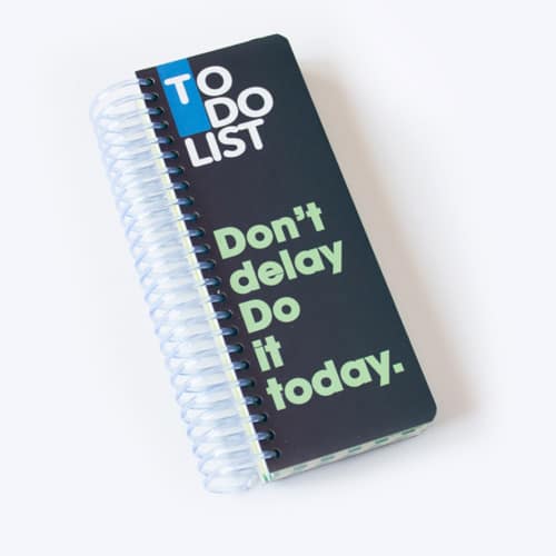 دفترچه یادداشت فهرست کارها با جلد مشکی، صحافی سیمی سفید و نوشته‌های انگلیسی «TO DO LIST» و «Don't delay, do it today».